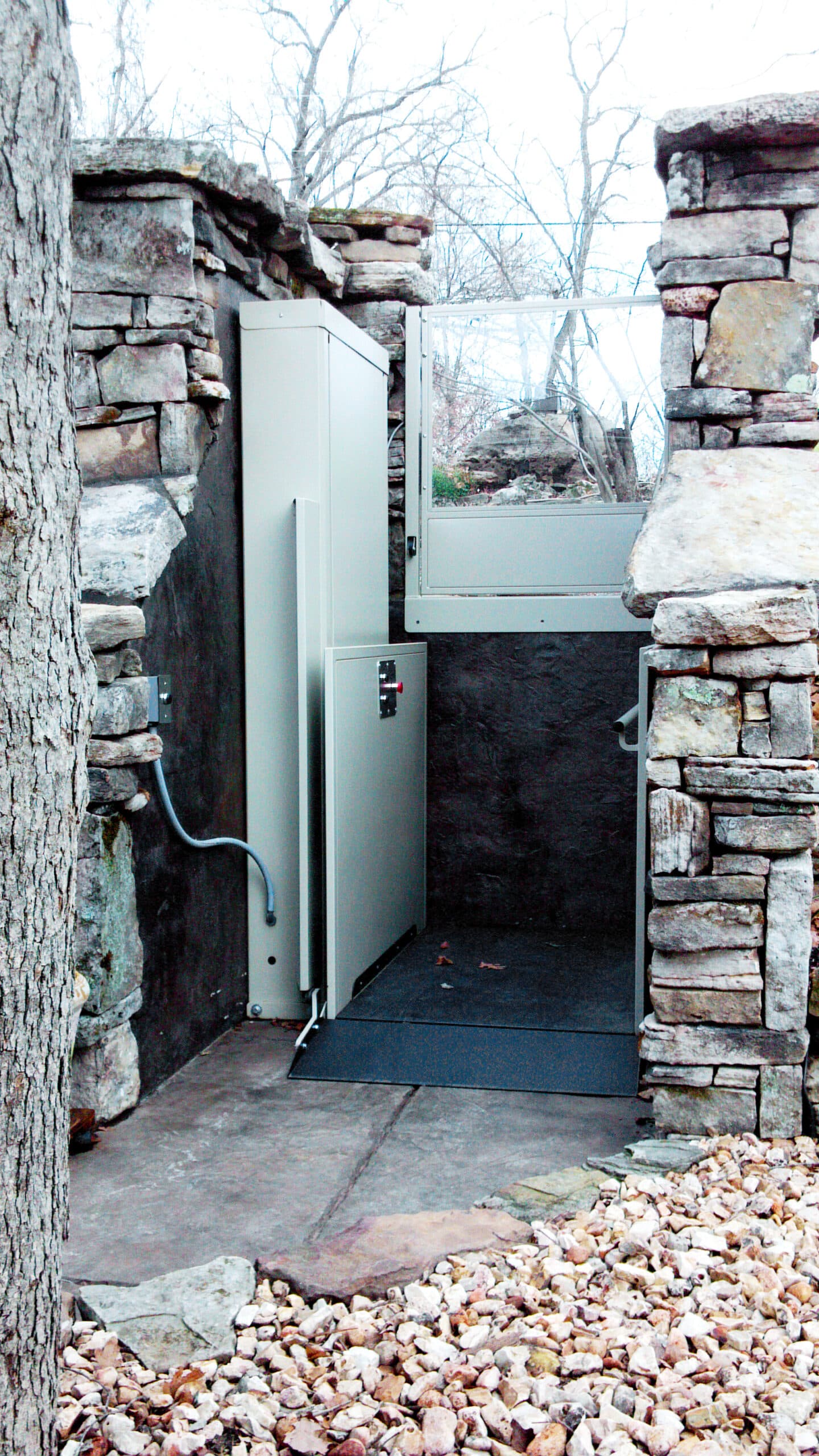 unenclosed vertical platform lift in outdoor setting with surrounding stone