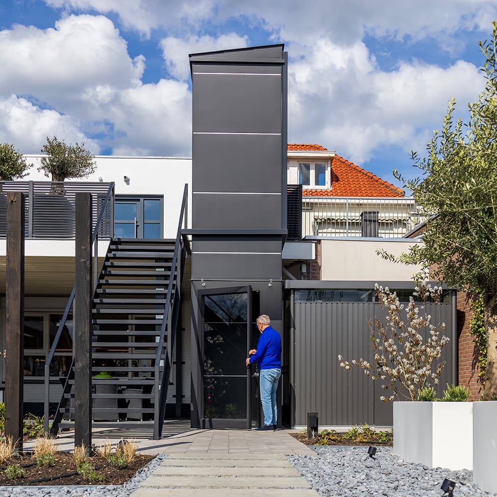 Balck Cibes outdoor platform lift in a garden with an grey-haired man in jeans a blue sweater.
